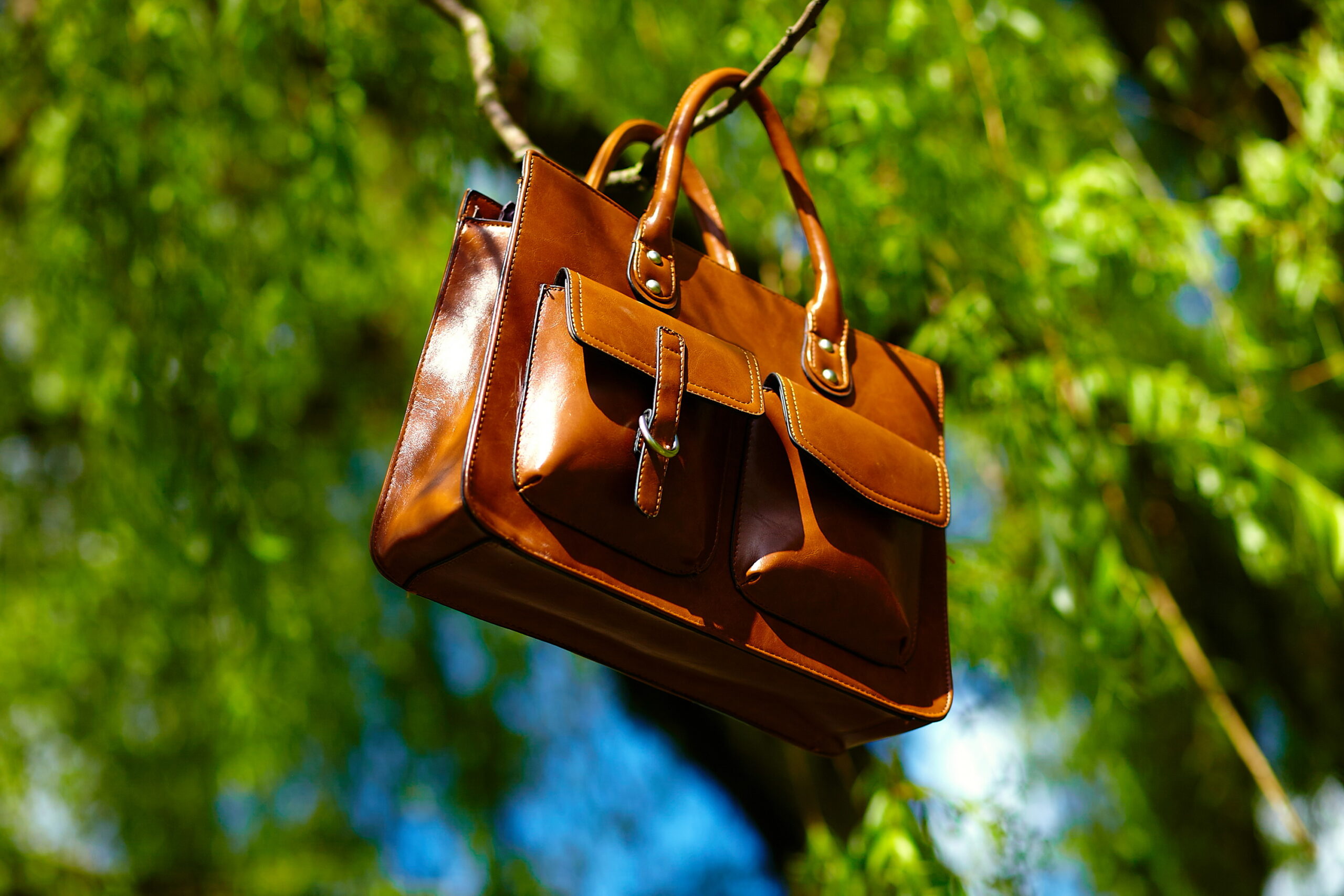 Home retro brown man leather bag in bright colorful summer park hanging on leafes